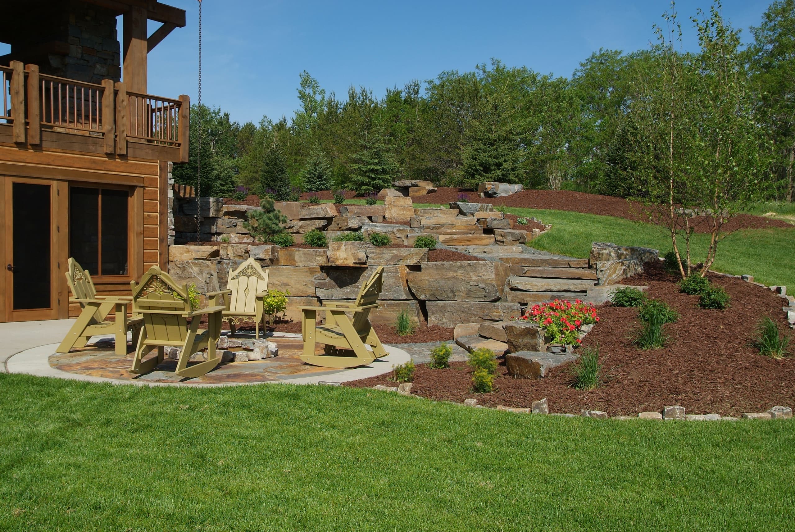 Massive stacked boulder retaining wall with Adirondack patio and fire pit